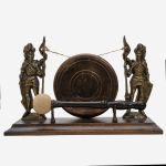 Gongo europeu em bronze e madeira, ladeado por figuras de cavalheiros medievais. Med.: 18 x 28 cm.