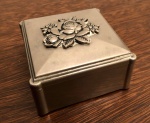 Pequena caixa porta joias, de metal prateado. Med. 08x08cm e 05cm de altura.