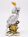 Escultura em porcelana alemã policromada, representando figura de cacatua empoleirada. Marcas no verso. Alemanha. 1922. 22 cm.